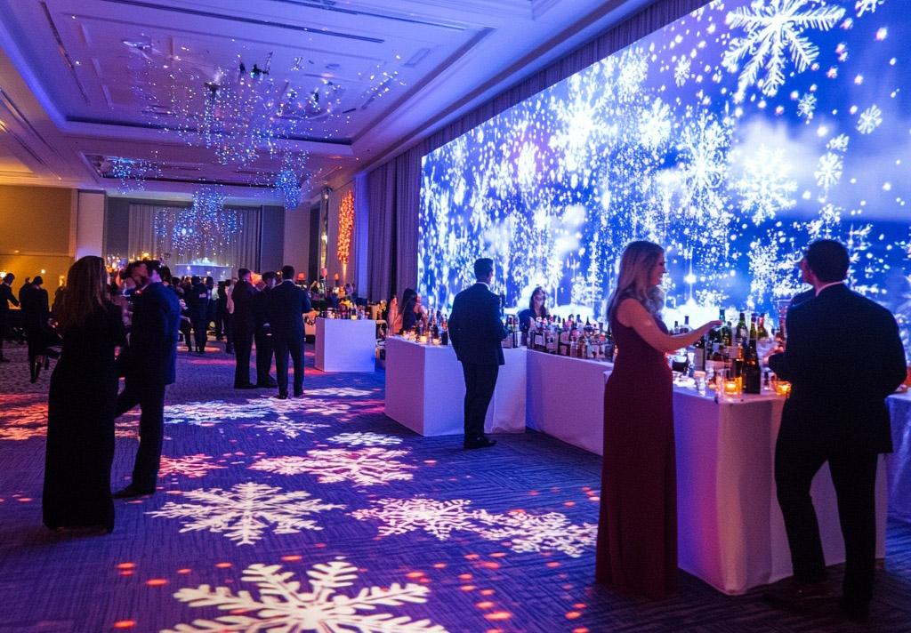 A formal event with guests in evening attire, standing by drink bars in a large room decorated with blue snowflake lights projected on the walls and floor, creating a winter-themed atmosphere.